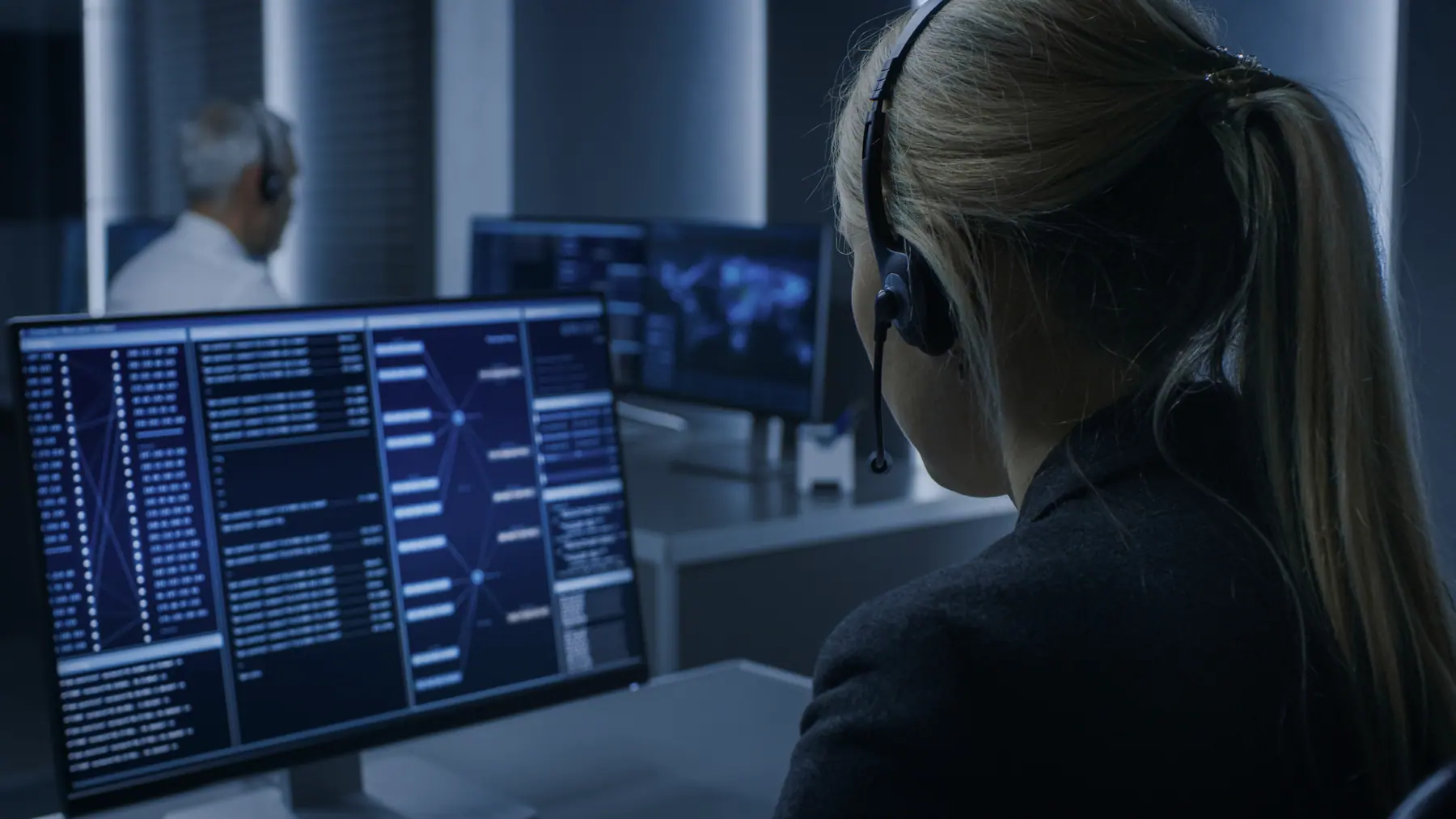 Technikerin mit Headset vor mehreren Monitoren im Leitstand